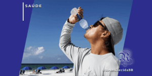 Homem ao ar livre em uma praia ensolarada bebendo água de uma garrafa plástica para se hidratar, representando a prevenção contra riscos cardíacos causados pelas altas temperaturas e ondas de calor.