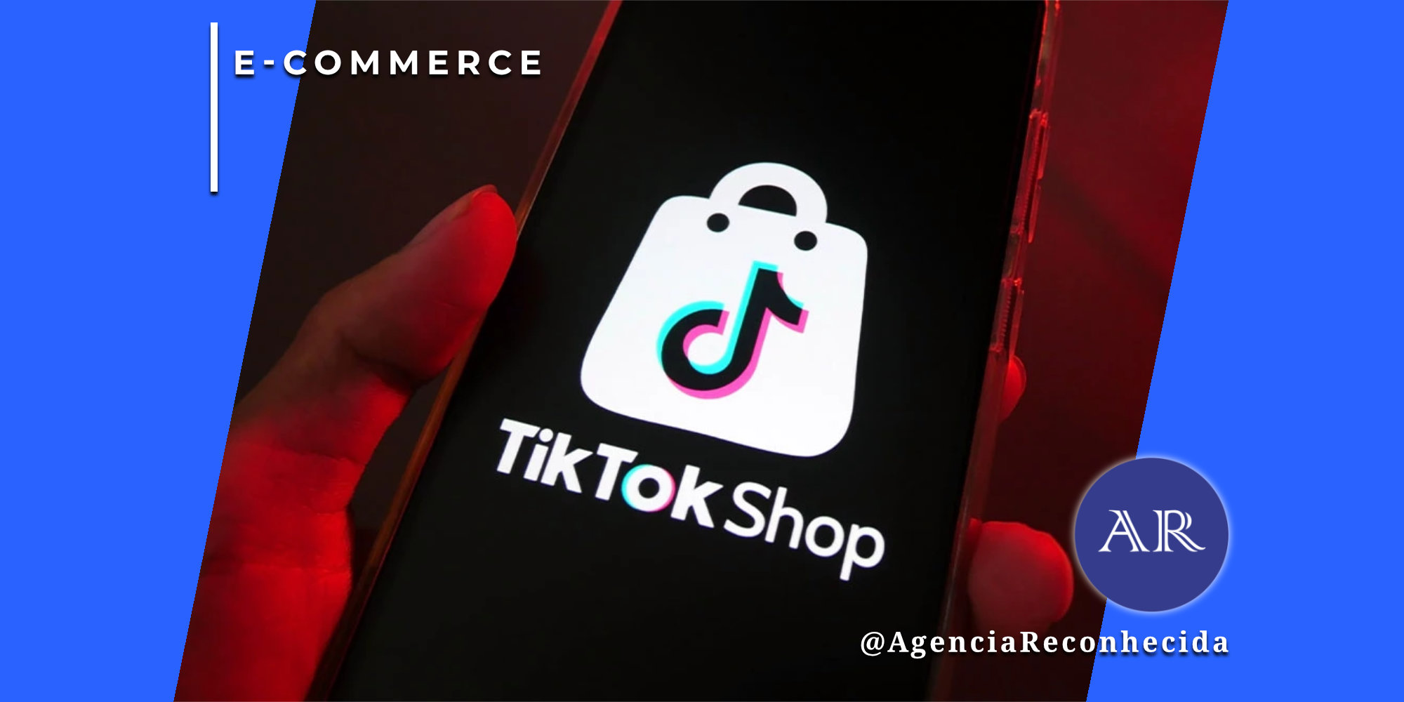 Mão segurando um smartphone que exibe o logotipo branco do TikTok Shop em uma tela preta. O logotipo consiste em uma sacola de compras com o símbolo musical icônico do TikTok no centro. No canto superior esquerdo, o selo 'E-COMMERCE' sobre fundo azul e, no inferior direito, o logotipo AR da Agência Reconhecida com o @AgenciaReconhecida.