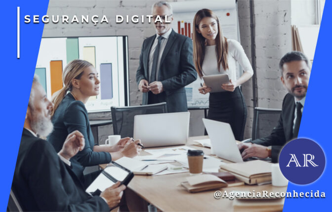 Grupo de executivos em uma sala de reuniões moderna discutindo dados em torno de uma mesa de madeira com notebooks e tablets. Ao fundo, telas exibem gráficos de barras coloridos. No canto superior esquerdo, o selo 'SEGURANÇA DIGITAL' sobre fundo azul e, no inferior direito, o logotipo AR da Agência Reconhecida com o @AgenciaReconhecida.