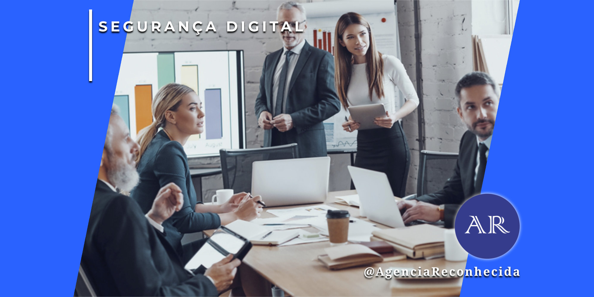 Grupo de executivos em uma sala de reuniões moderna discutindo dados em torno de uma mesa de madeira com notebooks e tablets. Ao fundo, telas exibem gráficos de barras coloridos. No canto superior esquerdo, o selo 'SEGURANÇA DIGITAL' sobre fundo azul e, no inferior direito, o logotipo AR da Agência Reconhecida com o @AgenciaReconhecida.