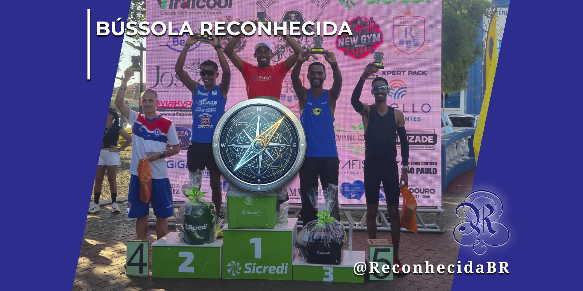 Cinco atletas masculinos de atletismo comemoram em um pódio numerado de um a cinco com a marca Sicredi, segurando pequenos troféus e cestas de premiação em um evento ao ar livre. Ao fundo, um painel rosa exibe logotipos de patrocinadores locais. No centro exato da imagem, há a ilustração sobreposta de uma bússola redonda com detalhes em azul e dourado apontando para o norte. No canto superior esquerdo, aparece o selo BÚSSOLA RECONHECIDA em letras brancas; no inferior direito, o logotipo do portal Reconhecida com o @ReconhecidaBR.