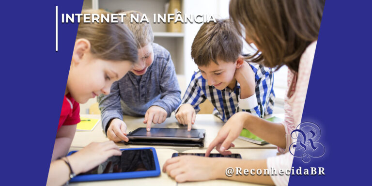 Grupo de quatro crianças, meninos e meninas, reunidas ao redor de mesas escolares interagindo e apontando para as telas de dois tablets digitais deitados. Elas aparecem sorridentes e focadas nos dispositivos. No canto superior esquerdo, há o selo INTERNET NA INFÂNCIA em letras brancas; no inferior direito, o logotipo do portal Reconhecida com o @ReconhecidaBR.