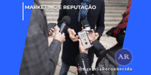 Uma pessoa ao centro vestindo casaco escuro e cachecol azul é abordada de perto por repórteres e jornalistas para uma entrevista na rua. Em primeiro plano, destacam-se as mãos dos repórteres segurando um microfone de reportagem preto, um gravador digital de áudio portátil e um smartphone que exibe na tela um aplicativo de gravador de voz ativo marcando 00:01:19. No canto superior esquerdo, aparece o selo MARKETING E REPUTAÇÃO em letras brancas; no canto inferior direito, destaca-se o logotipo redondo AR com o @AgenciaReconhecida.