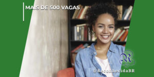 Uma mulher jovem negra e sorridente, com cabelos cacheados e vestindo camisa jeans aberta sobre uma blusa clara, sentada em uma poltrona vermelha. Ao fundo, há uma estante repleta de livros de forma levemente desfocada e uma parede rústica à esquerda. No topo esquerdo, destaca-se o texto "Mais de 500 Vagas" e, no canto inferior direito, o logotipo clássico do portal Reconhecida com a assinatura @ReconhecidaBR.