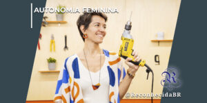 Mulher sorridente com cabelos curtos segura uma furadeira elétrica amarela em uma oficina com ferramentas ao fundo. No topo esquerdo, o texto "Autonomia Feminina" e, no canto inferior direito, o logotipo do portal Reconhecida com a marca d'água @ReconhecidaBR.