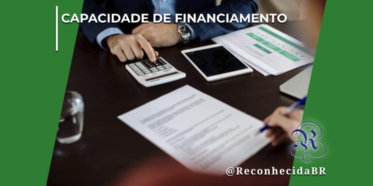 Vista superior parcial de duas pessoas em uma reunião de negócios ao redor de uma mesa de madeira escura. Uma das pessoas opera uma calculadora branca com a mão esquerda, enquanto a outra segura uma caneta azul pronta para assinar um documento em primeiro plano. Na mesa há um tablet digital, relógio de pulso e folhas com gráficos verdes. No topo esquerdo, lê-se o texto "Capacidade de Financiamento" e, no canto inferior direito, o logotipo do portal Reconhecida com a assinatura @ReconhecidaBR.