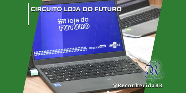 Um notebook preto aberto sobre uma mesa de madeira, exibindo na tela o logotipo azul com o texto "loja do FUTURO" e os logotipos da Fecomércio SP e do Sebrae. Ao fundo, parcialmente visíveis, há outro notebook e documentos. No canto inferior direito, o logotipo clássico do portal Reconhecida com a assinatura @ReconhecidaBR.