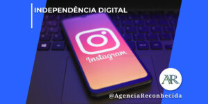 martphone escuro apoiado sobre o teclado de um notebook, exibindo na tela o logotipo clássico do Instagram em destaque com fundo avermelhado e roxo, em um ambiente corporativo escuro. No canto superior esquerdo, lê-se o texto "Independência Digital". No canto inferior direito, o logotipo redondo com as letras "AR" e a assinatura @AgenciaReconhecida.