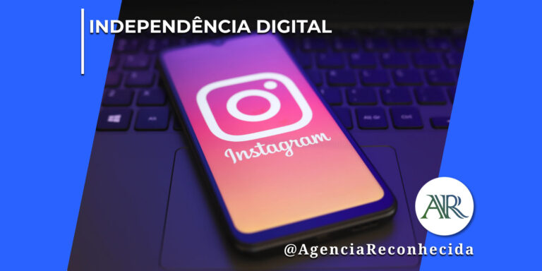 martphone escuro apoiado sobre o teclado de um notebook, exibindo na tela o logotipo clássico do Instagram em destaque com fundo avermelhado e roxo, em um ambiente corporativo escuro. No canto superior esquerdo, lê-se o texto "Independência Digital". No canto inferior direito, o logotipo redondo com as letras "AR" e a assinatura @AgenciaReconhecida.